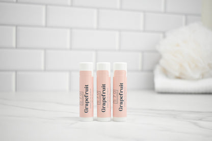 Three lip balm tubes labeled 'Grapefruit' on a bathroom counter with a tiled wall background.