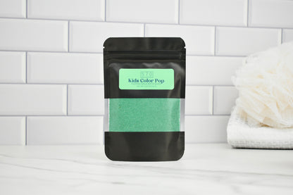 Black pouch with green powder labeled 'Kids Color Pop' on a white tiled background