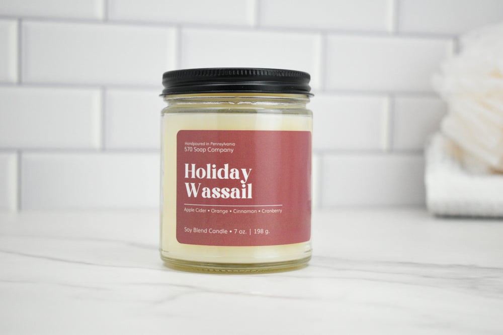 Candle jar labeled 'Holiday Wassail' on a white surface with a tiled wall background