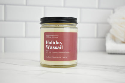 Candle jar labeled 'Holiday Wassail' on a white surface with a tiled wall background