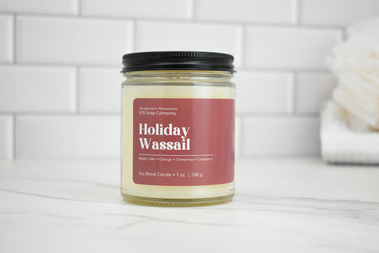 Candle jar labeled 'Holiday Wassail' on a white surface with a tiled wall background