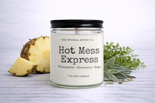 Candle labeled 'Hot Mess Express' with a pineapple and greenery on a light background