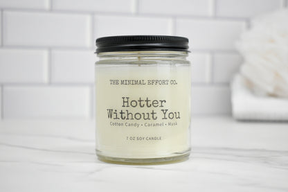Candle jar labeled 'Hotter Without You' by The Minimal Effort Co. on a white surface with a tiled wall background.