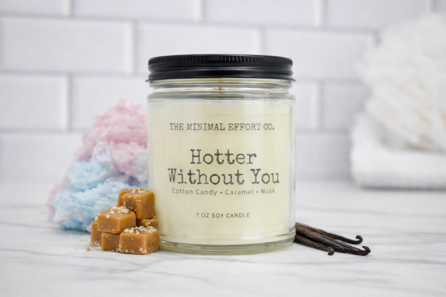 Candle jar labeled 'Hotter Without You' by The Minimal Effort Co. on a white surface with decorative items.