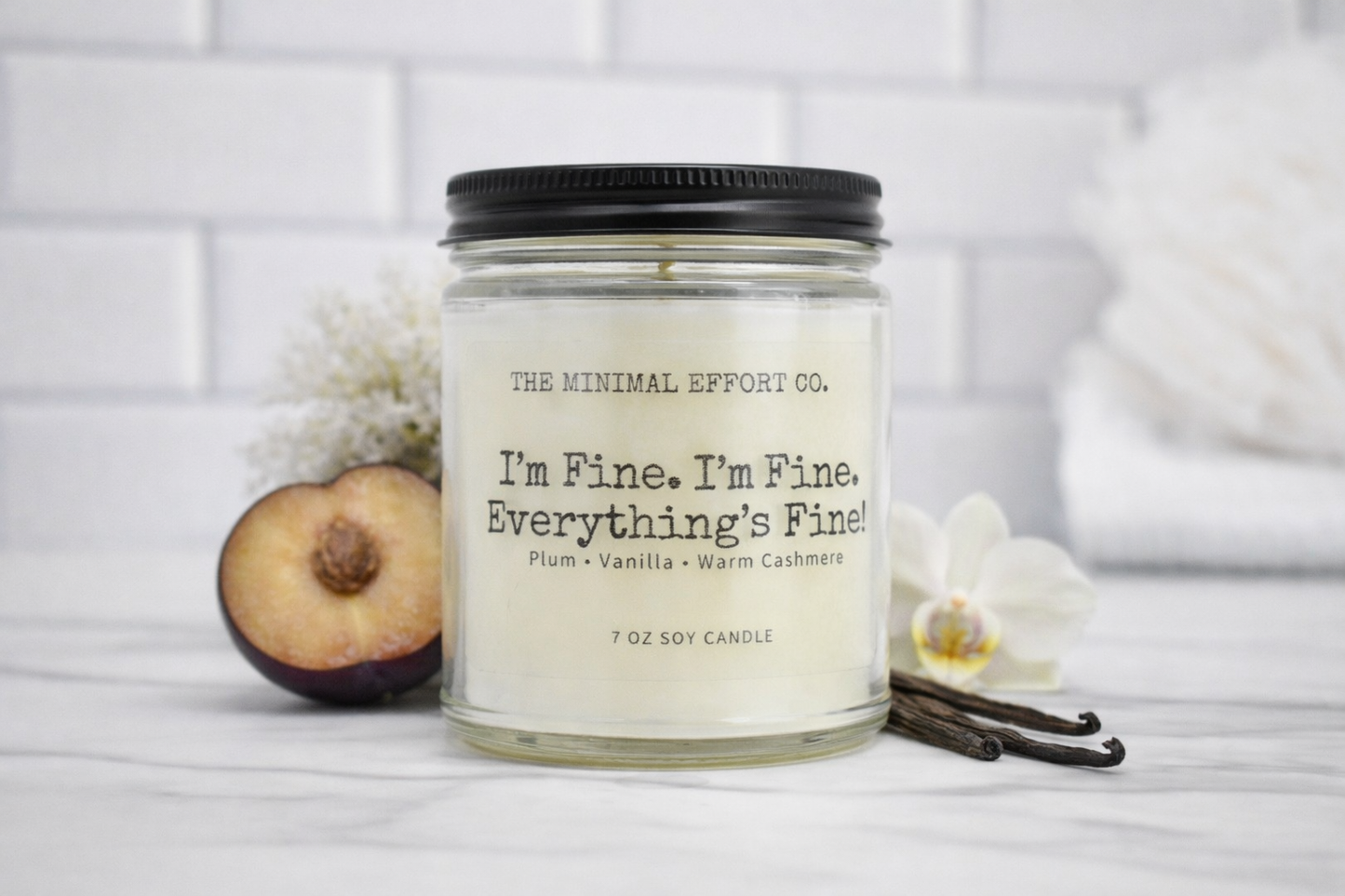 Candle jar with 'The Minimal Effort Co.' branding and text on a white surface with peaches and vanilla beans.