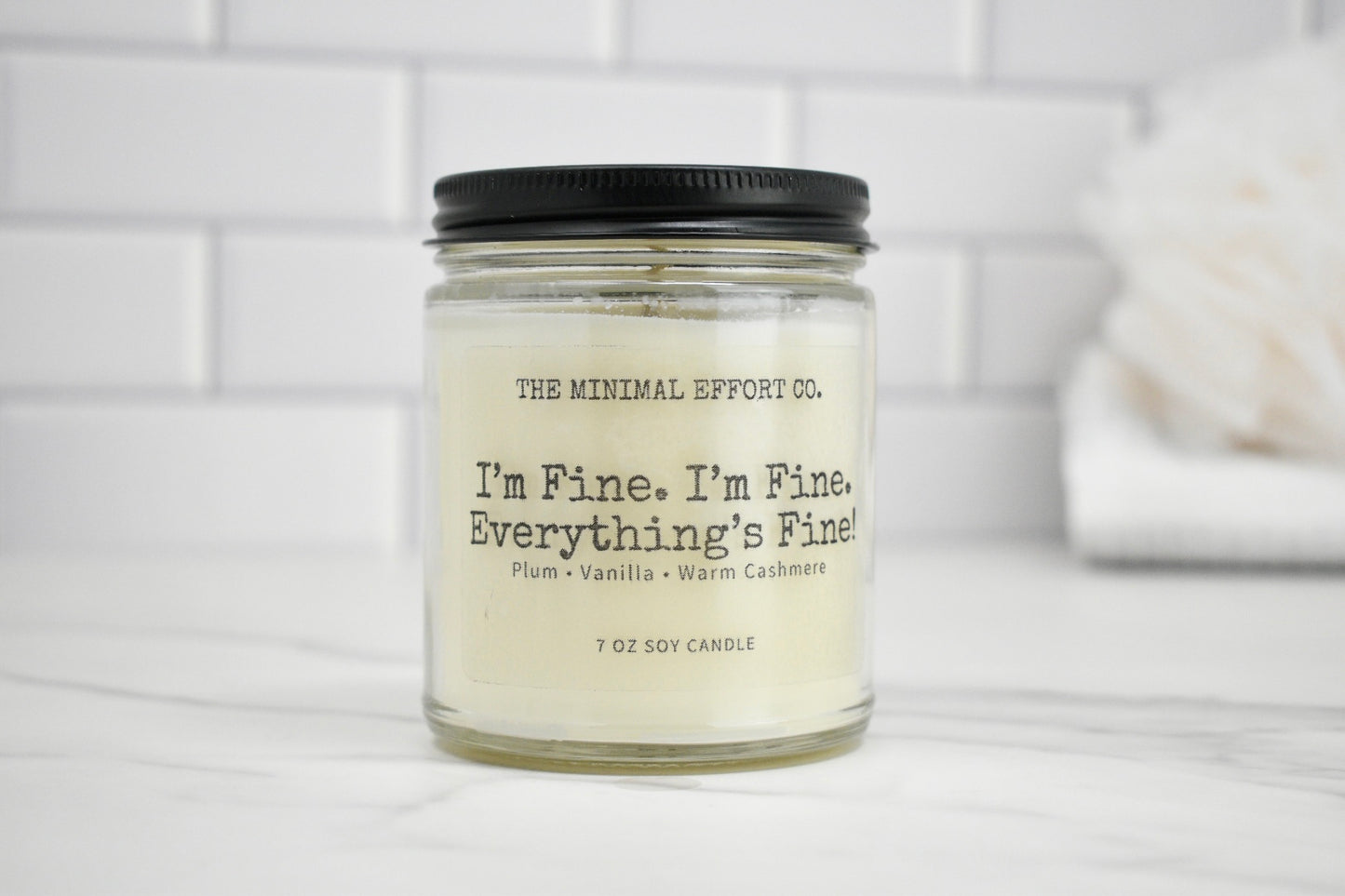 Candle jar with label on a white surface and tiled wall background