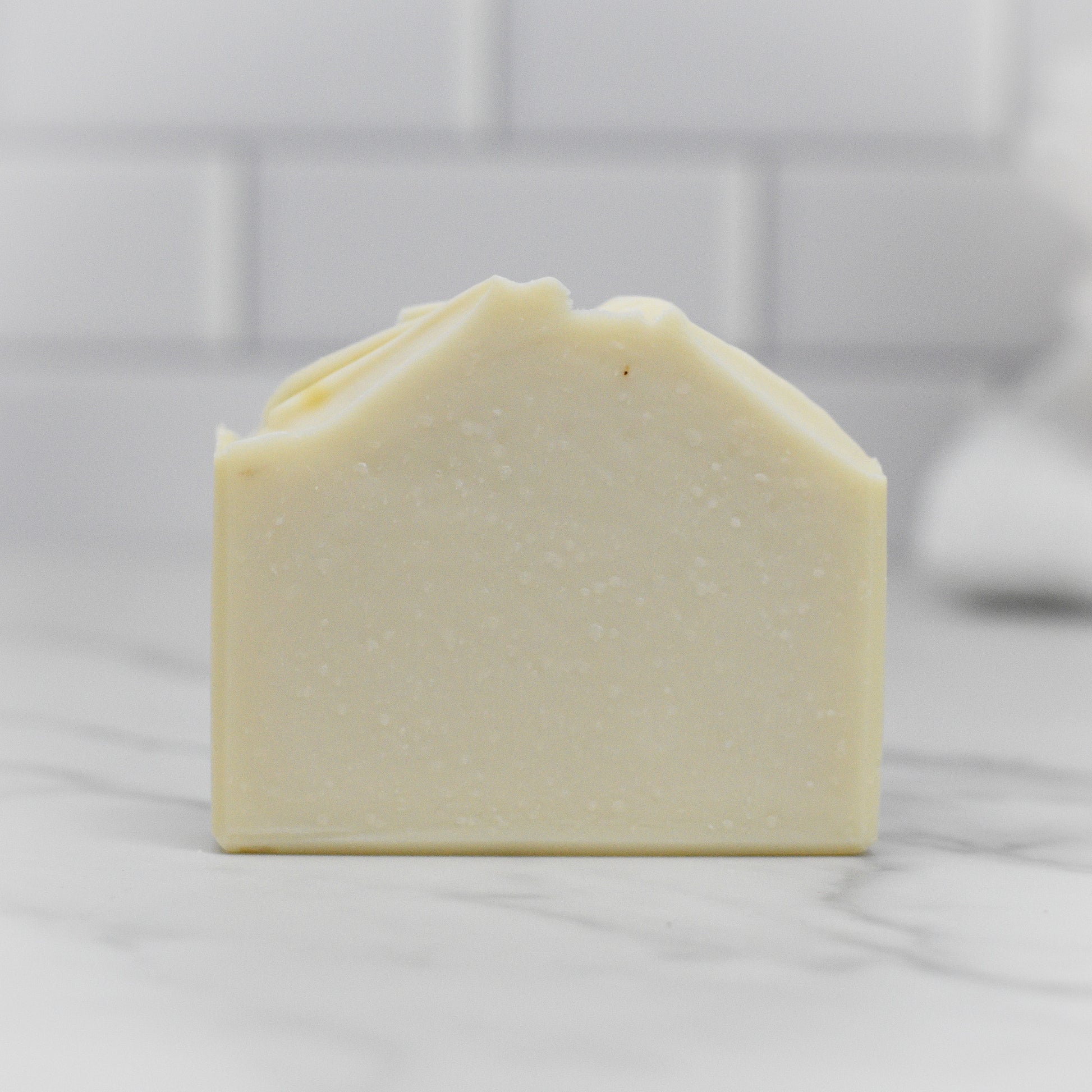 A close-up of the Jewelweed Infused Bar Soap - All Natural by 570 Soap Co. showcases its smooth, creamy texture. Made with enriching coconut oil, it sits elegantly on a marble surface against a backdrop of white tiles.