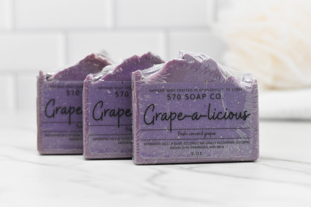 Three Juicy Grape Delight Bar Soaps from 570 Soap Co., infused with nourishing olive oil. The packaging highlights the Fresh Concord Grape scent, displayed on a white surface against a tiled backsplash.