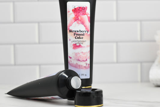 Two tubes of 570 Soap Co.'s Strawberry Pound Cake Lightweight Lotion are pictured against a white tiled background. One stands upright while the other lies horizontally with the cap off, showcasing a creamy, dessert-like image on the packaging.