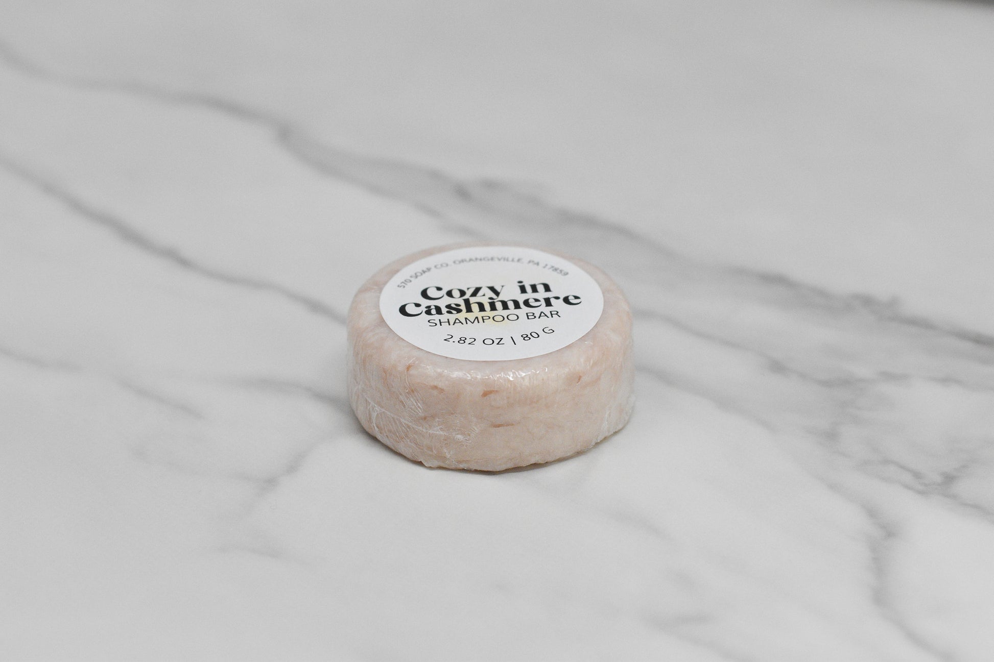 The Cozy in Cashmere Shampoo Bar by 570 Soap Co. is an eco-friendly product that promises luxurious hair care and features a distinctive round design with its label.