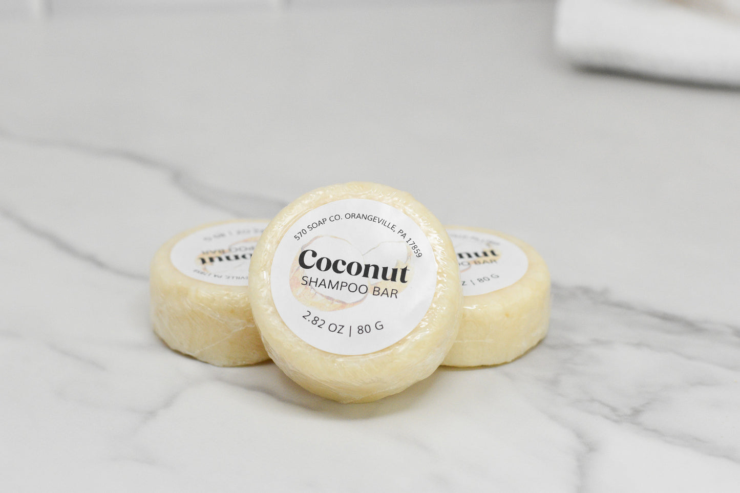 Three wrapped Coconut Shampoo Bars from 570 Soap Co., each infused with a tropical coconut fragrance, are elegantly placed on a marble surface—an eco-friendly hair care solution that brings the essence of the tropics to your daily routine.