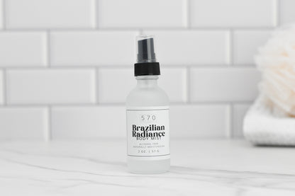 A bottle of Luxurious Fragranced Body Mist Spray by 570 Soap Co. stands against a white tiled background. The label prominently features "Alcohol-Free with Naturally Hydrating Technology" and indicates the size as 2 oz / 57 g. To the right, a blurred item, likely a sponge, complements the tranquil scene.