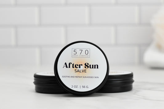 A small jar of 570 Soap Co.'s After Sun Salve is positioned against a minimalist white tile background. The label reads "After Sun Salve - Soothe and Repair Sun-Kissed Skin" with the contents listed as 2 oz / 56 g.