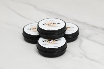 Four black plastic containers of After Sun Salve by 570 Soap Co. are placed on a white marble surface, with each container holding 2 oz (56 g) of soothing and repairing formula for sun-kissed skin.