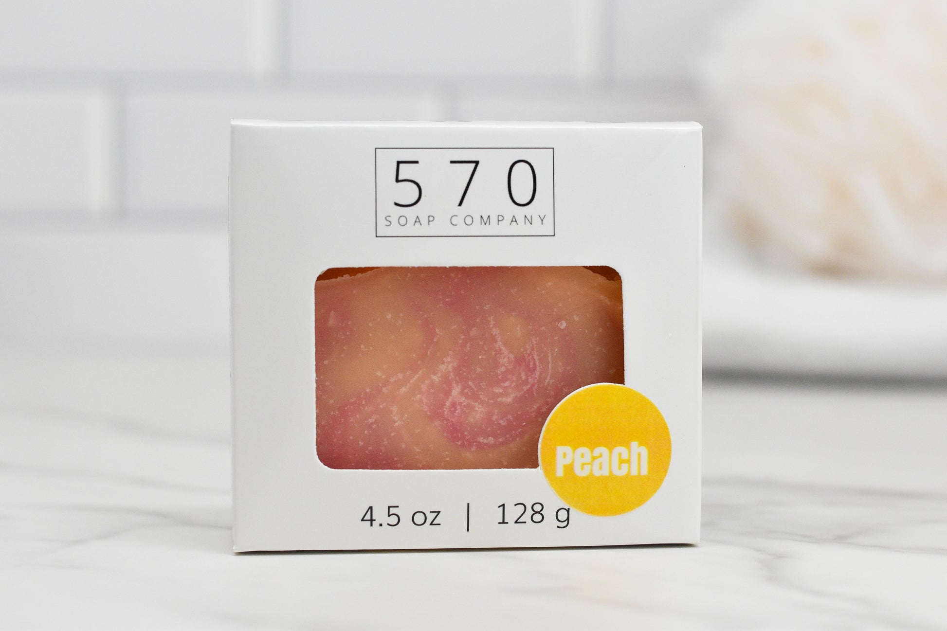 A bar of Perfectly Peach Bar Soap: Exotic Fusion in a white box bearing the 570 Soap Co. logo is visible through the packaging's window. A small yellow circle highlights its skin-pampering formula, and the box lists the weight as 4.5 oz (128 g).