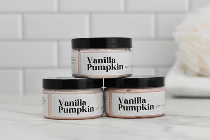 Three jars of 570 Soap Co.'s Vanilla Pumpkin Body Butter - SEASONAL are elegantly arranged on a marble surface. Promising hydration, the jars are stacked with two at the base and one perched on top. In the background, a blurred, fluffy towel lies against a tiled wall.