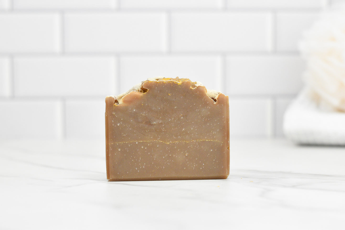 A bar of Frankincense & Myrrh soap from 570 Soap Co., showcasing artisanal craftsmanship with a rustic texture, sits on a marble surface. The background features white subway tiles and a blurred, white, fluffy object, evoking the timeless aromas of Frankincense and Myrrh.