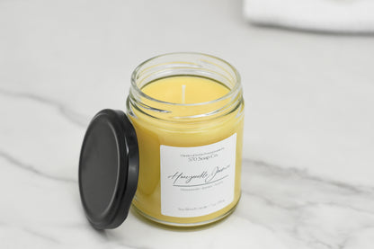 A Honeysuckle Jasmine Soy Blend Candle by 570 Soap Co. sits on a marble surface with a black lid. The Honeycomb label suggests a floral elegance, featuring yellow wax ideal for adding warmth to any room.