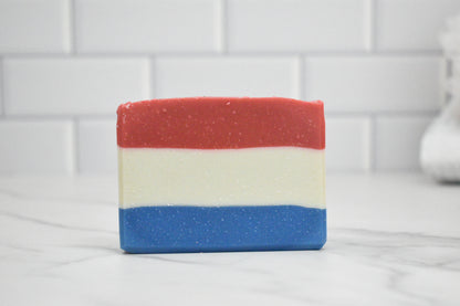 Three-layered soap bar with red, white, and blue stripes on a white tiled background