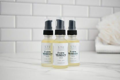 Three bottles of 570 Extra Moisture Serum on a bathroom counter with a tiled wall background.
