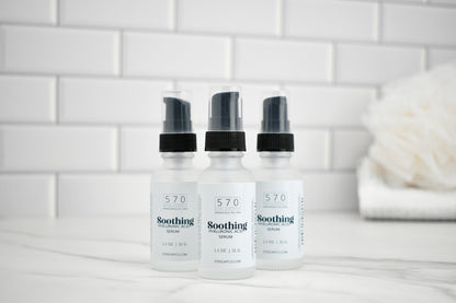 Three bottles of 570 Soothing Serum on a bathroom counter with a tiled wall background.