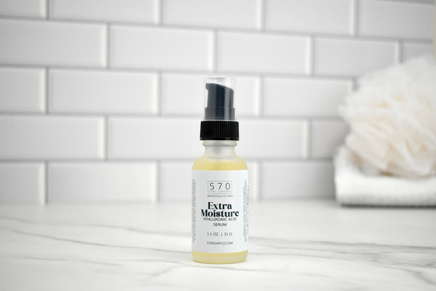 Bottle of 570 Extra Moisture Serum on a bathroom counter with a white tiled wall background.