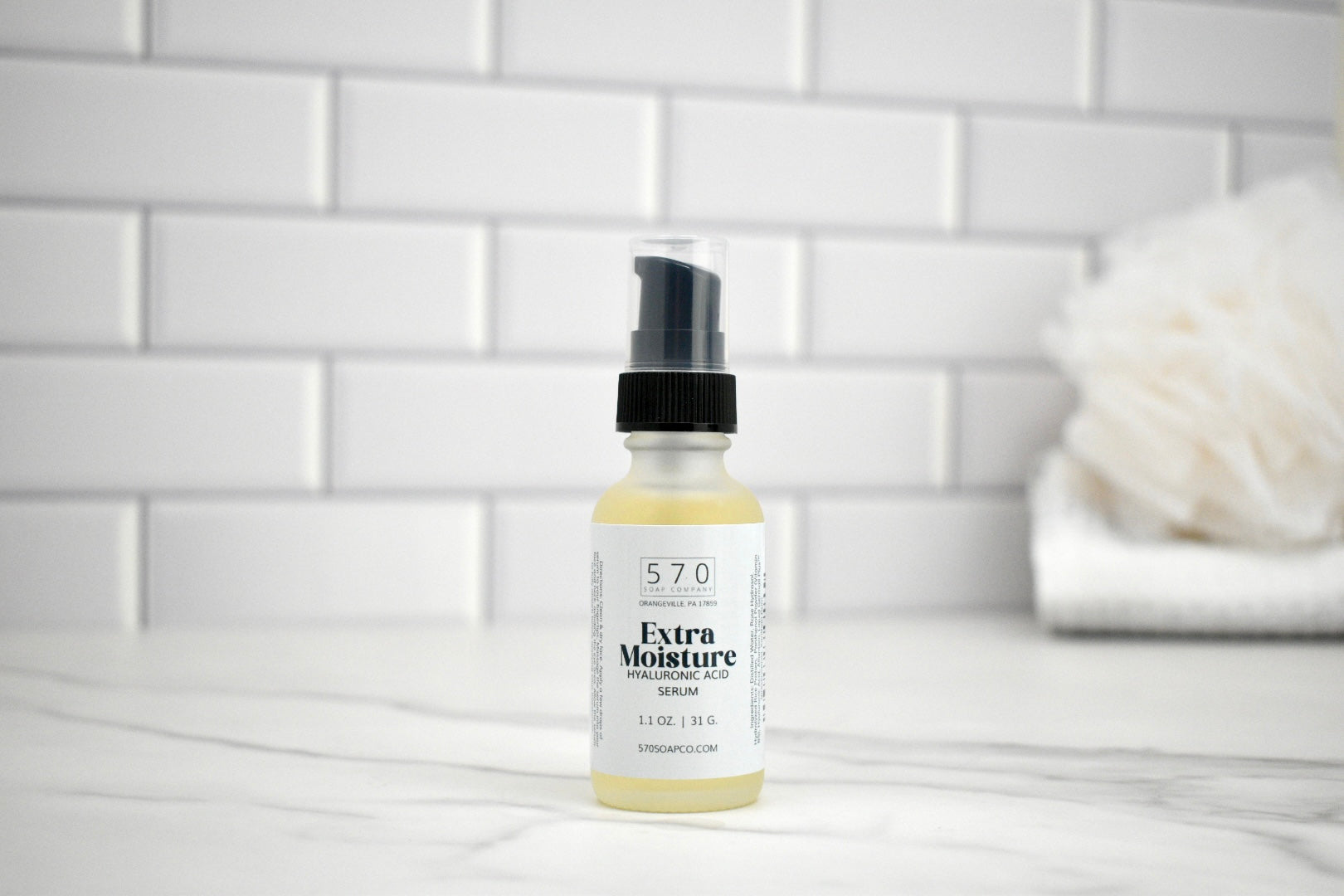 Bottle of 570 Extra Moisture Serum on a bathroom counter with a white tiled wall background.