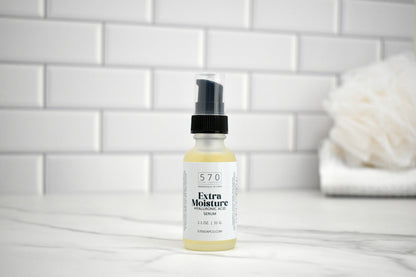 Bottle of 570 Extra Moisture Serum on a bathroom counter with a white tiled wall background.