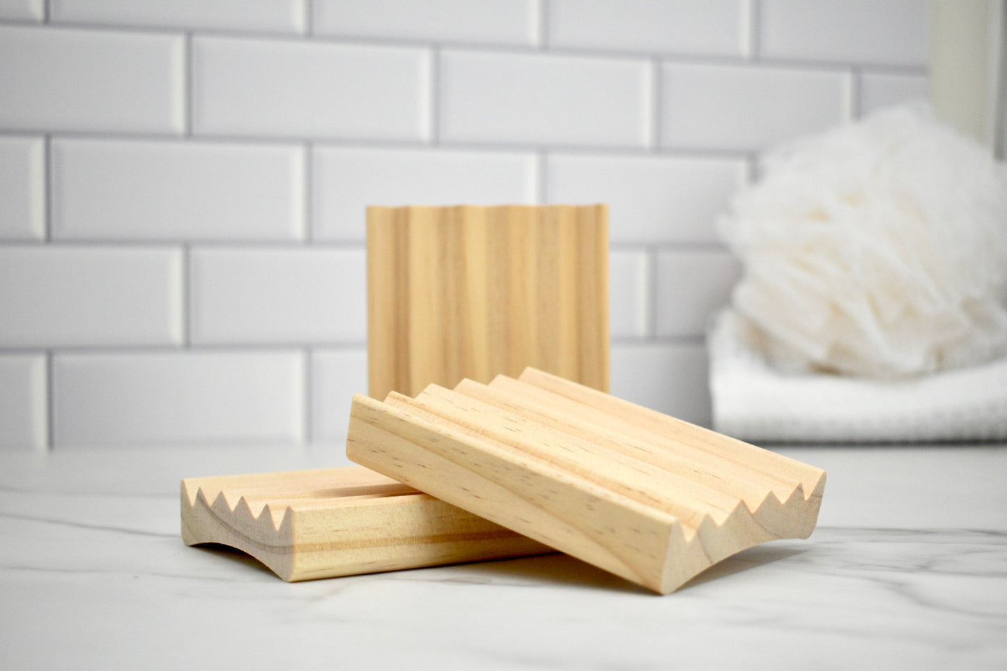 Three wooden soap dishes on a white surface with a tiled wall background