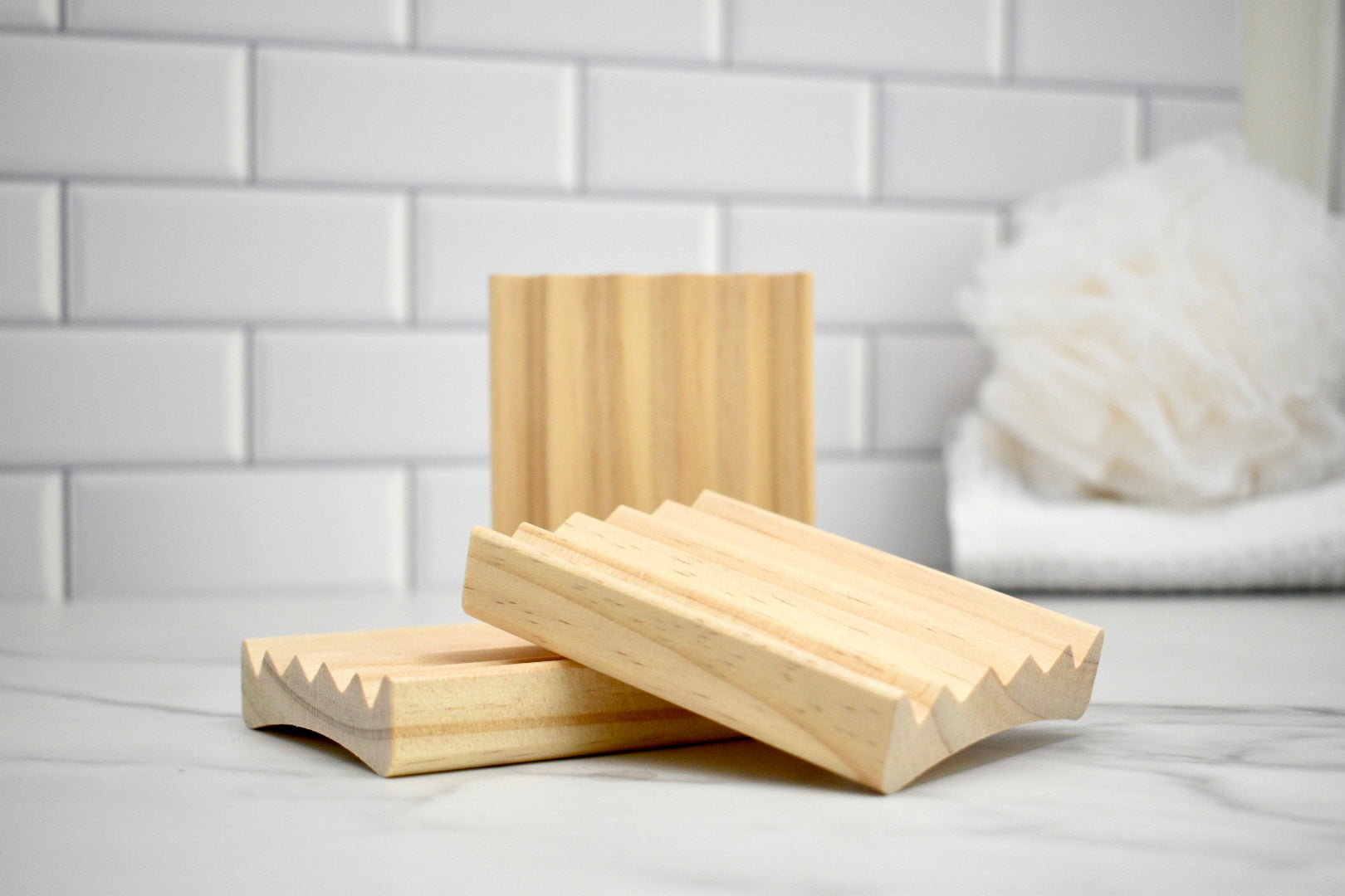 Three wooden soap dishes on a white surface with a tiled wall background