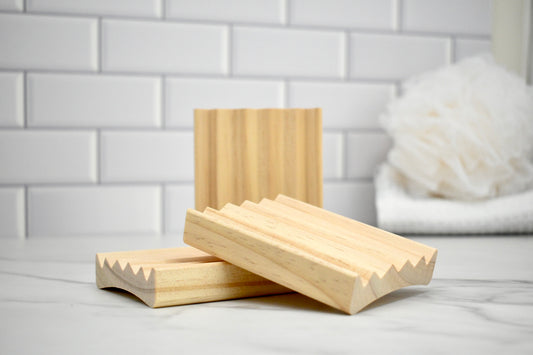 Three wooden soap dishes on a white surface with a tiled wall background