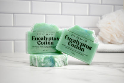 Three bars of Eucalyptus Cotton soap from 570 Soap Co on a white surface with a tiled wall background.