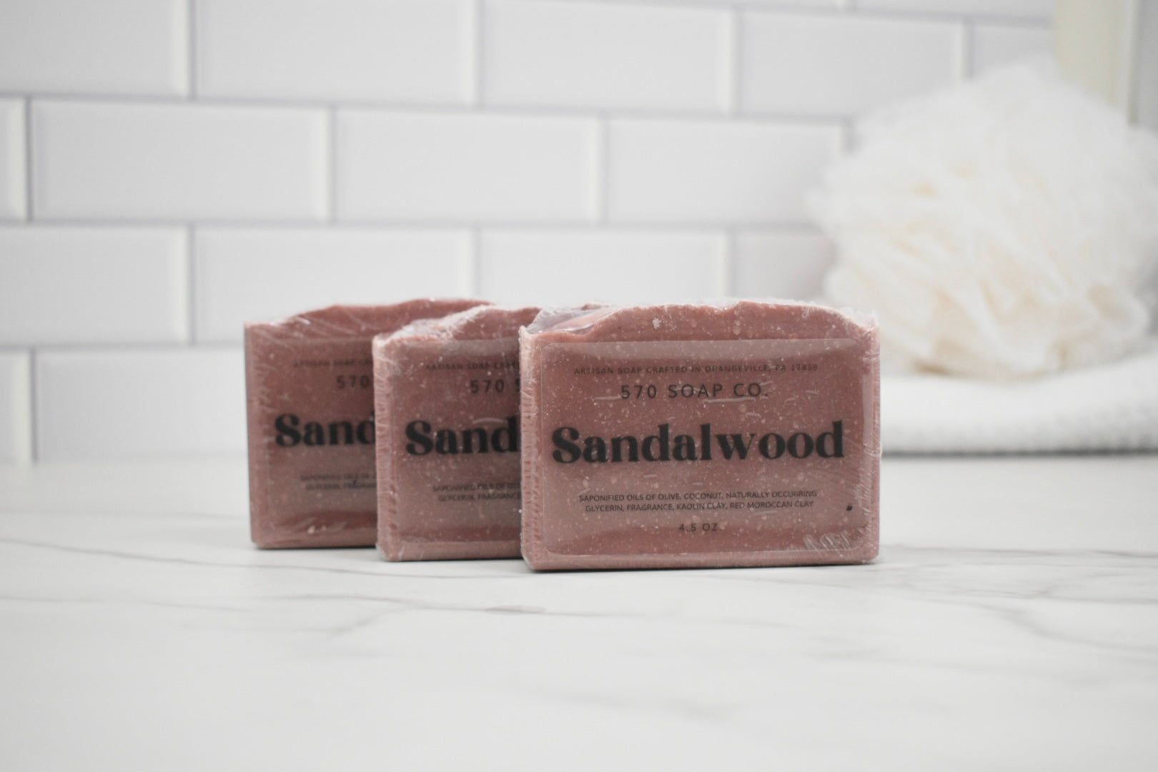 Three bars of Sandalwood soap from 570 Soap Co on a white surface with a tiled wall background.