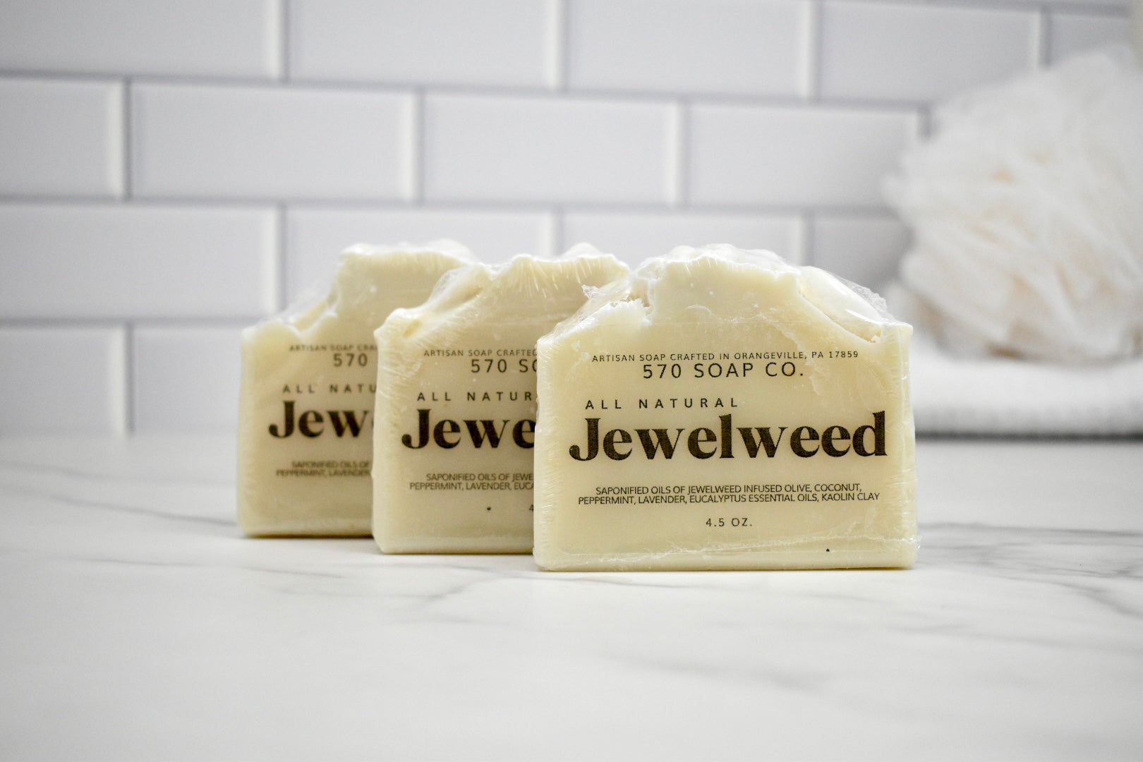 Three bars of Jewelweed soap from 570 Soap Co on a white surface with a tiled wall background.