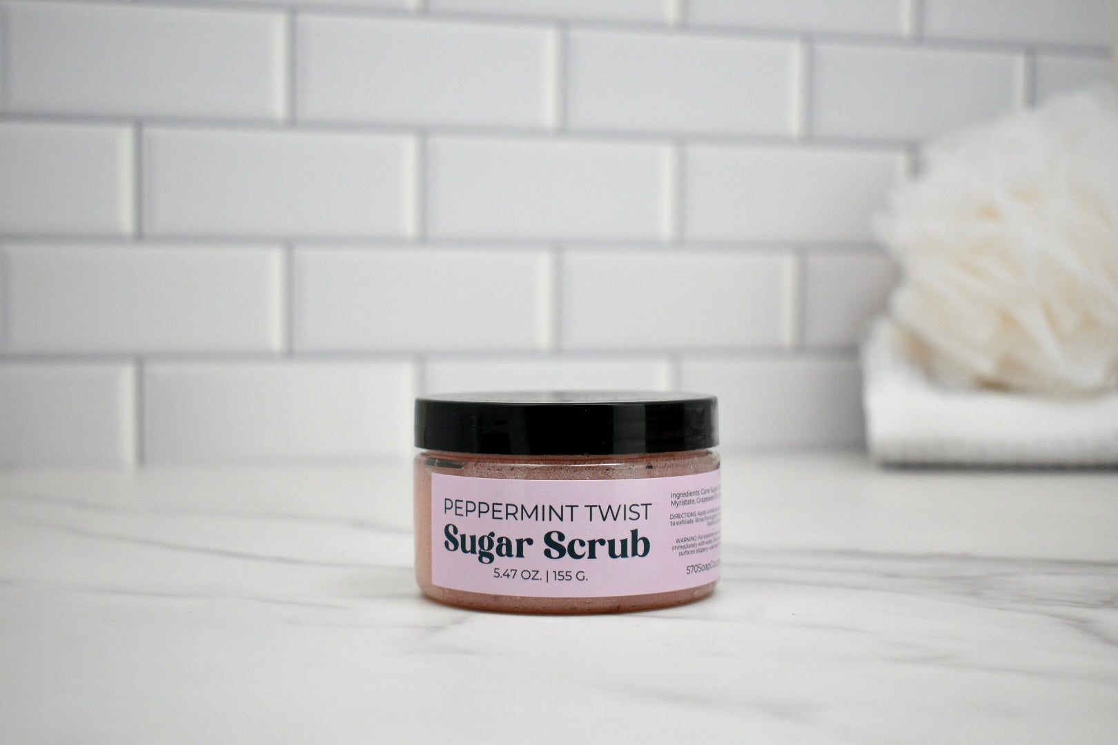 Jar of peppermint twist sugar scrub on a bathroom counter with a tiled wall background