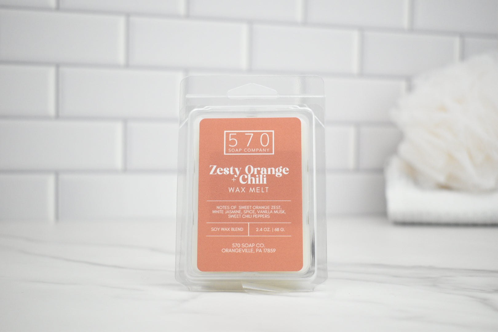 Zesty Orange Cream wax melt packaging on a white surface with a tiled wall background