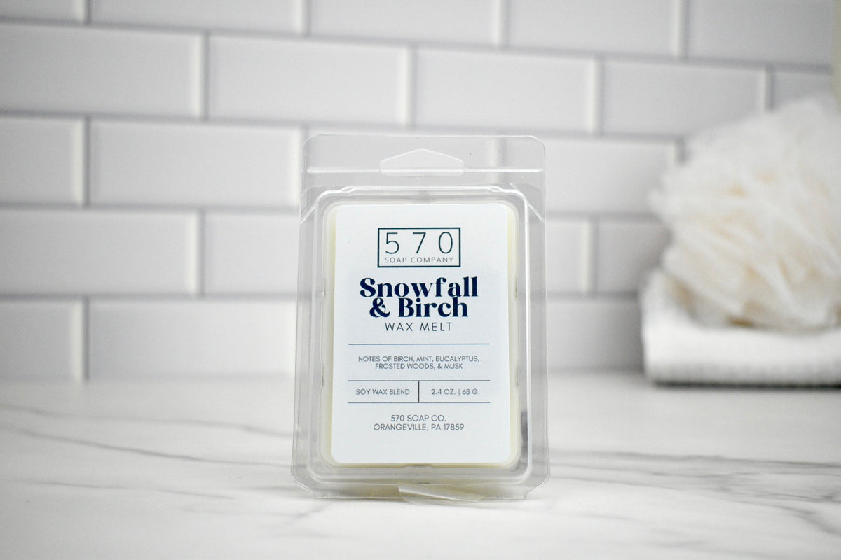 570 Snowfall & Birch wax melt packaging on a marble surface with a white tiled wall background