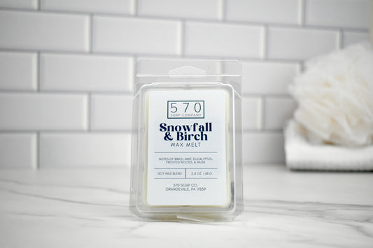 570 Snowfall & Birch wax melt packaging on a marble surface with a white tiled wall background