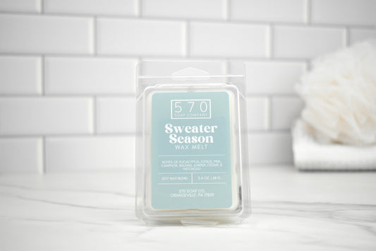 Wax melt packaging labeled 'Sweater Season' on a white surface with a tiled wall background.