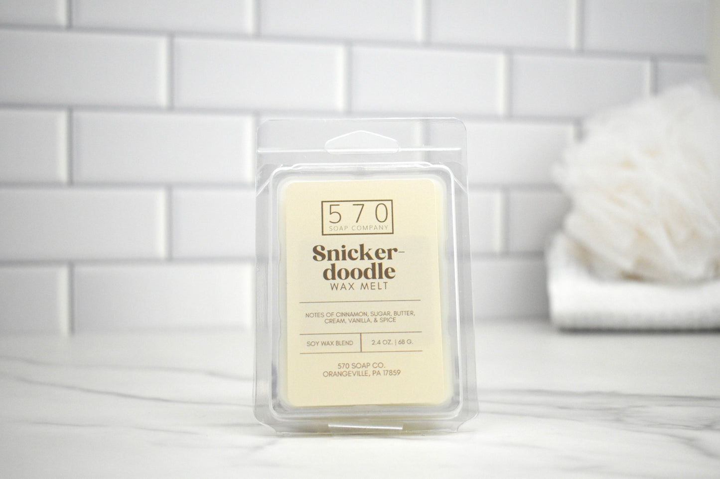 Snickerdoodle wax melt packaging on a white surface with a tiled wall background