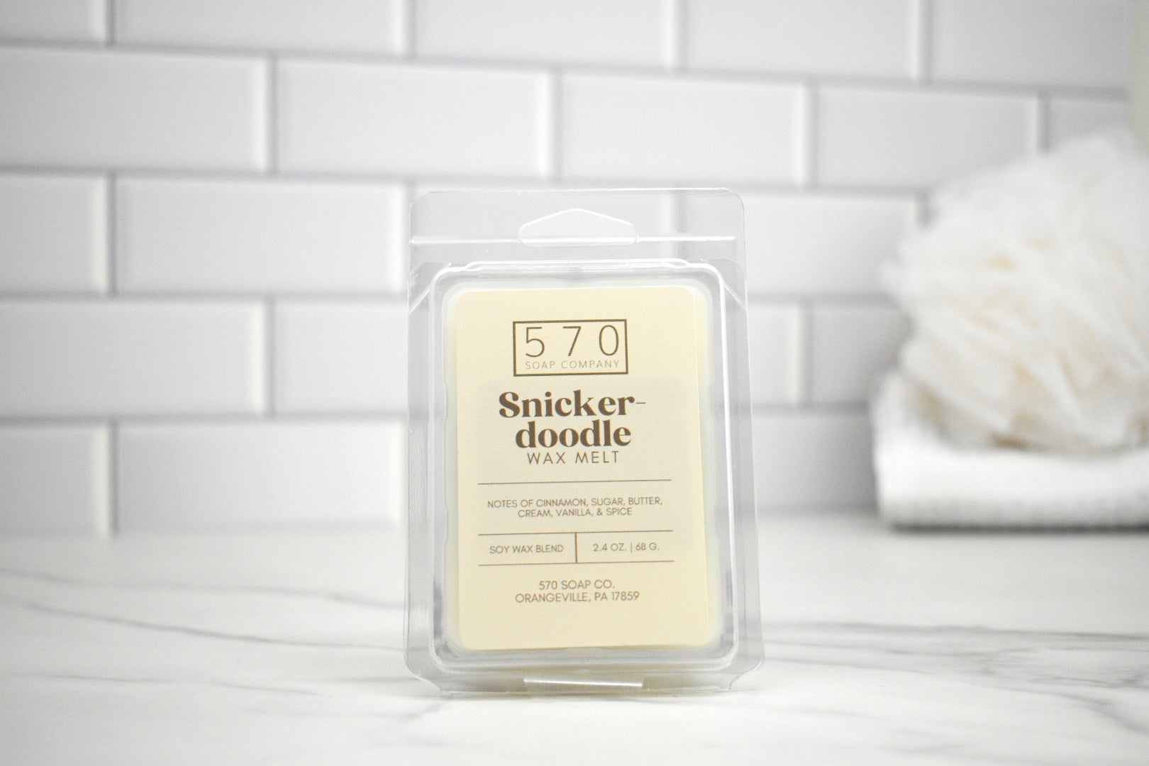 Snickerdoodle wax melt packaging on a white surface with a tiled wall background