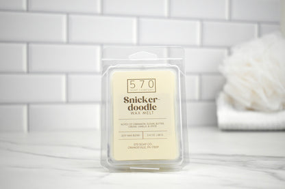 Snickerdoodle wax melt packaging on a white surface with a tiled wall background