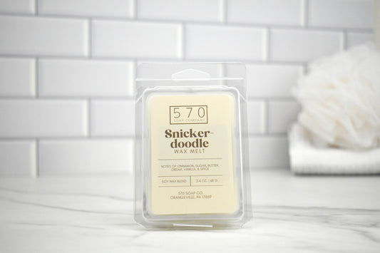 Snickerdoodle wax melt packaging on a white surface with a tiled wall background