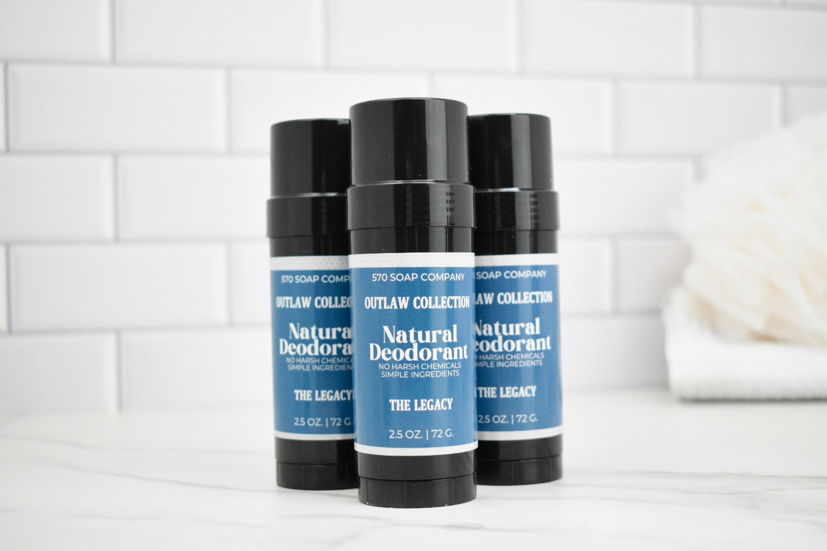 Three natural deodorant sticks from Outlaw Soap Company on a white tiled background