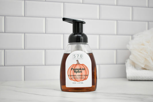 Bottle of pumpkin spice foaming hand soap on a bathroom counter with a tiled wall background.