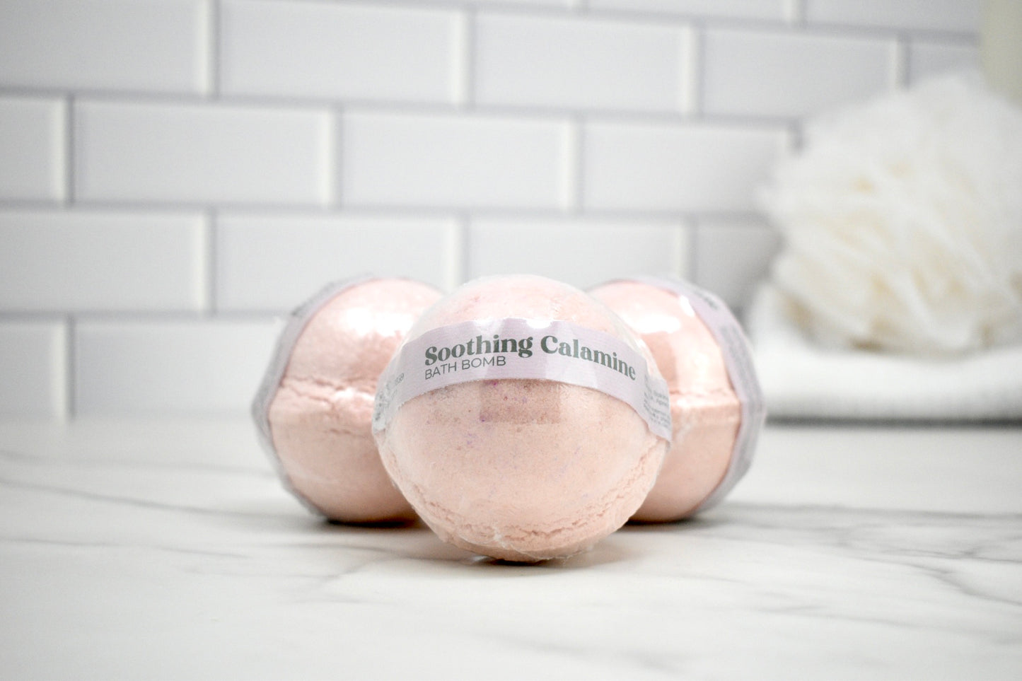 Bath bombs labeled 'Soothing Calamine' on a bathroom counter with a tiled wall background.