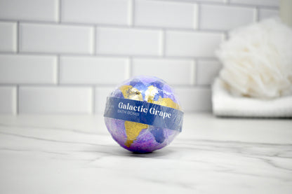 Bath bomb labeled 'Galactic Grape' on a tiled bathroom floor.