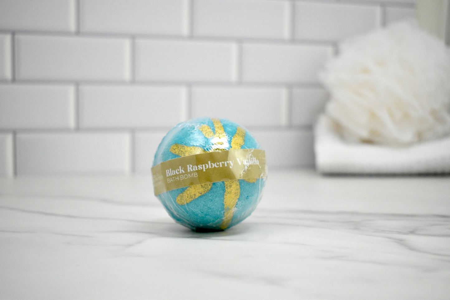 Blue and gold bath bomb on a bathroom counter with a tiled wall background