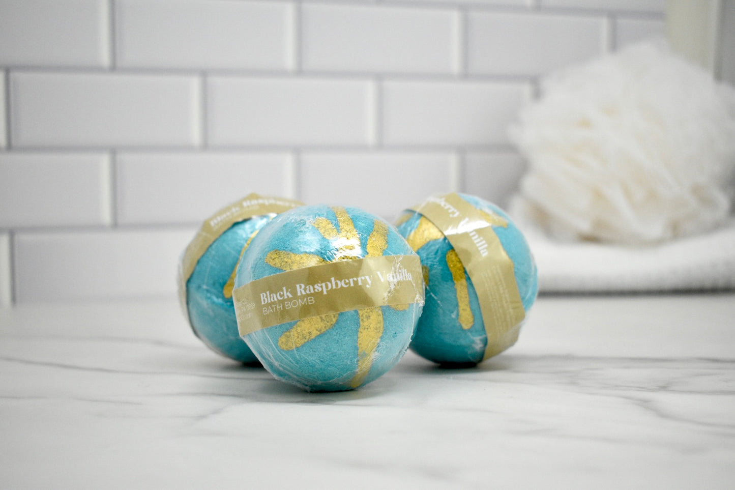 Threebath bombs with blue and gold packaging on a tiled bathroom floor.