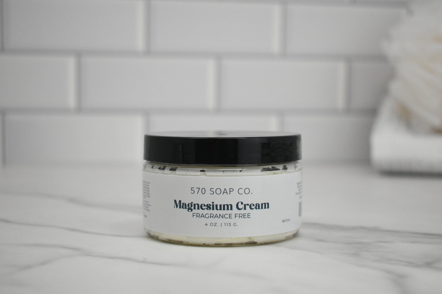 Jar of 570 Soap Co. Magnesium Cream on a marble surface with tiled wall background